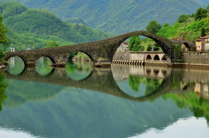 Мост поражает своей непривычной формой, а отражение на поверхности реки создает его подводного брата-близнеца.